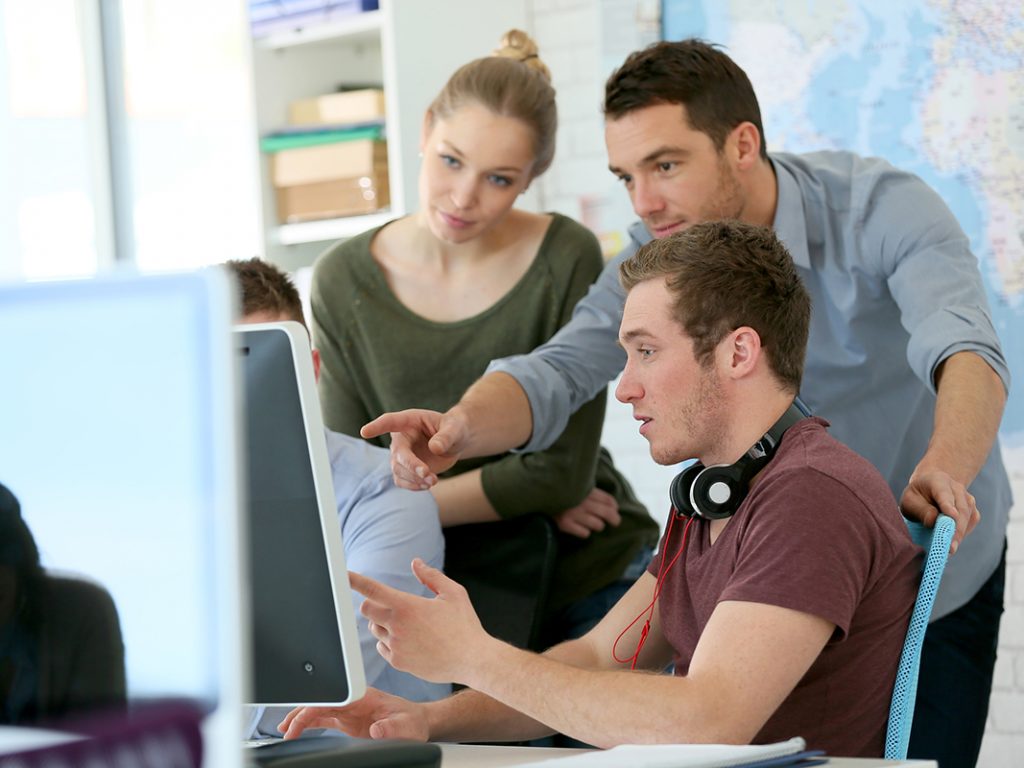 Drei junge Menschen sitzen und stehen vor einem Computerbildschirm