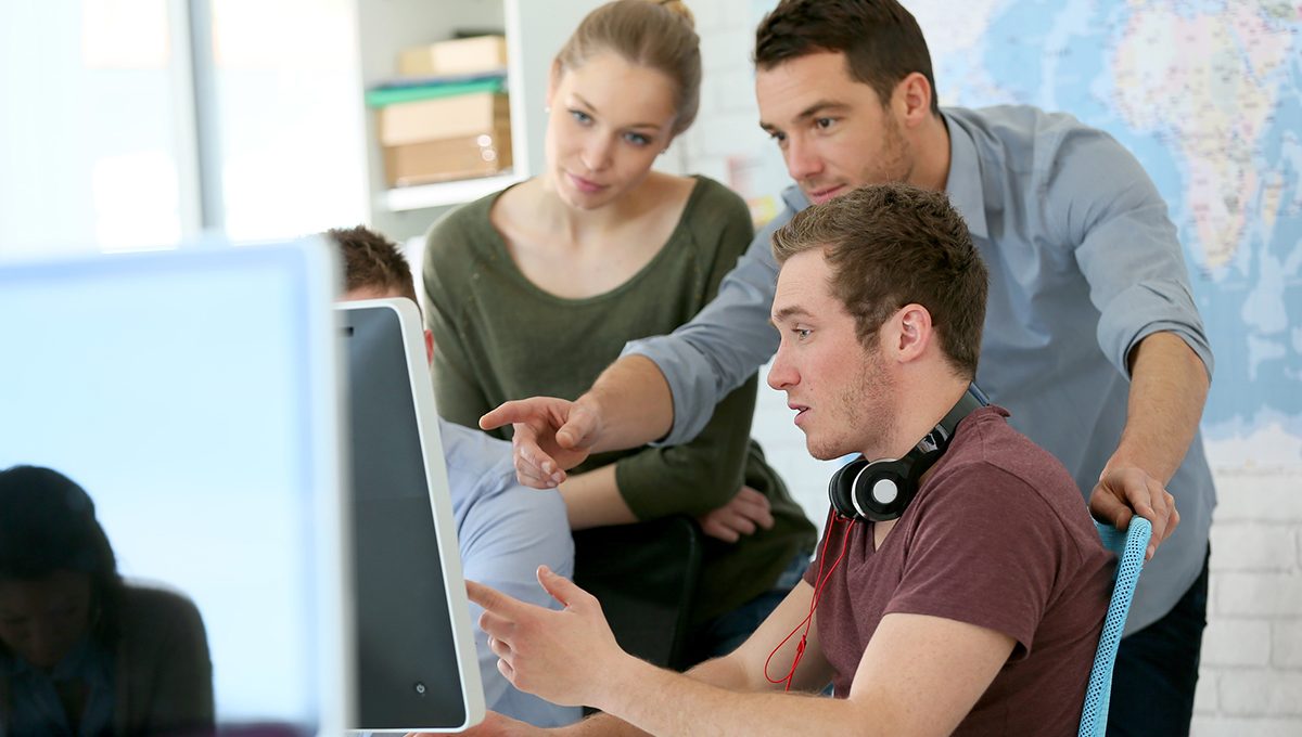 Drei junge Menschen sitzen und stehen vor einem Computerbildschirm