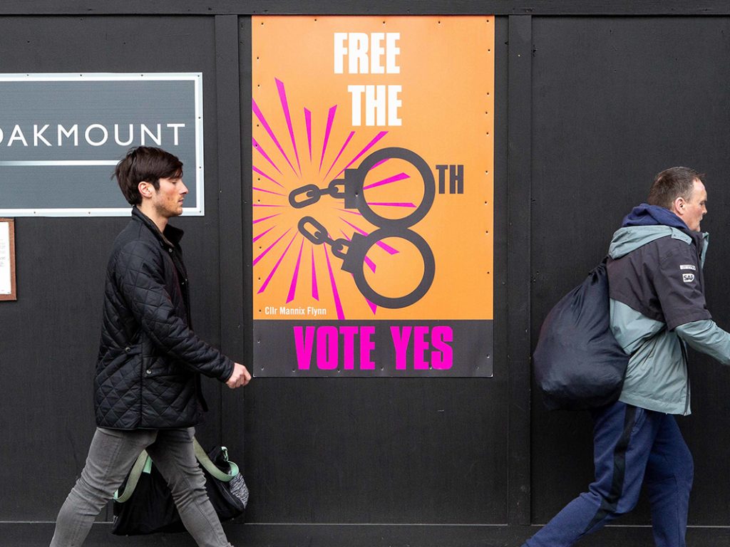 Passanten gehen an einem Plakat vorbei, auf dem dafür geworben wird, beim Referendum für die Abschaffung des Verfassungszusatzes zum Abtreibungsverbot zu stimmen.